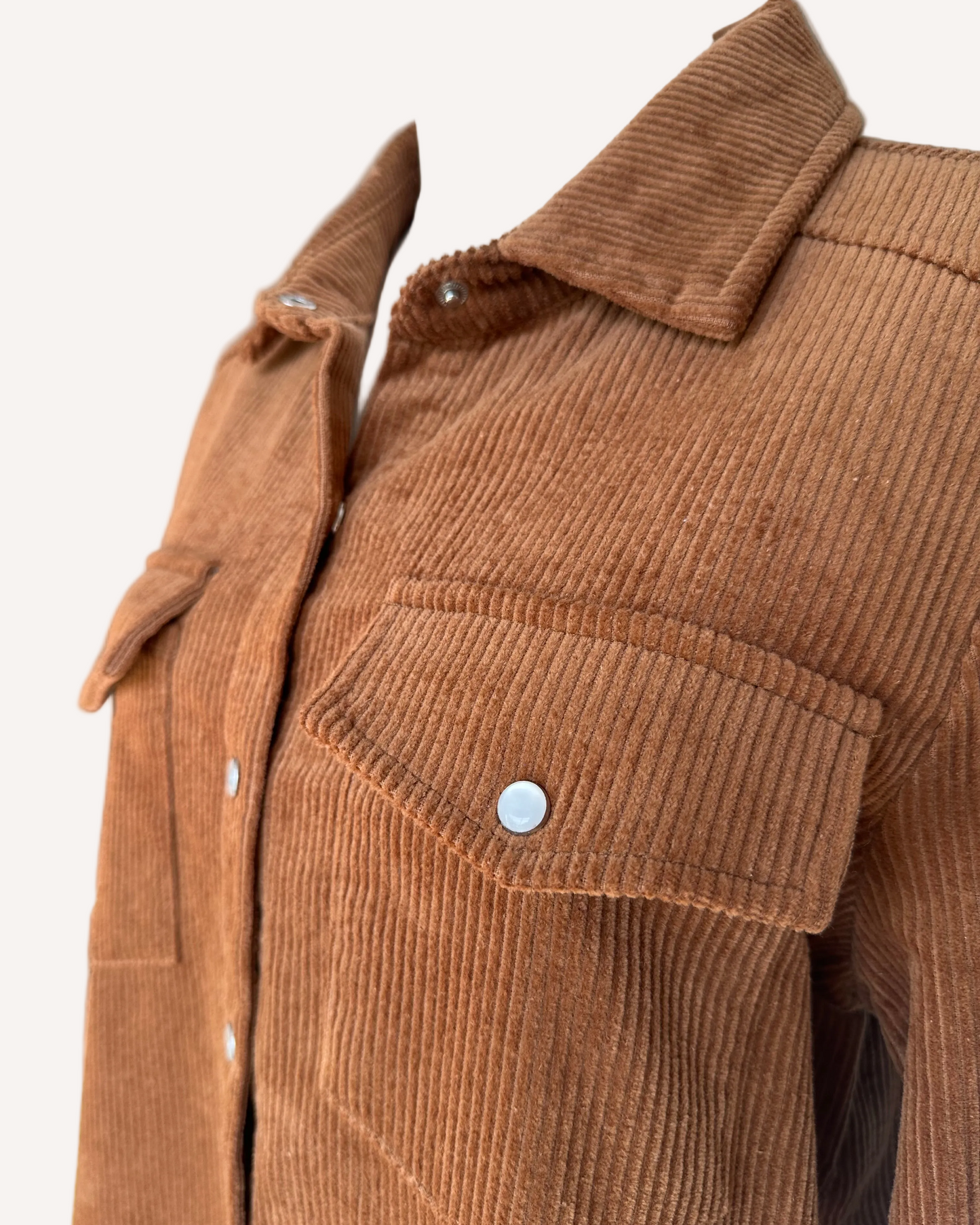 Soft corduroy button-down shacket with a relaxed fit and side pockets, shown in a neutral tone against a clean soft-linen background, styled as a cozy layering piece.