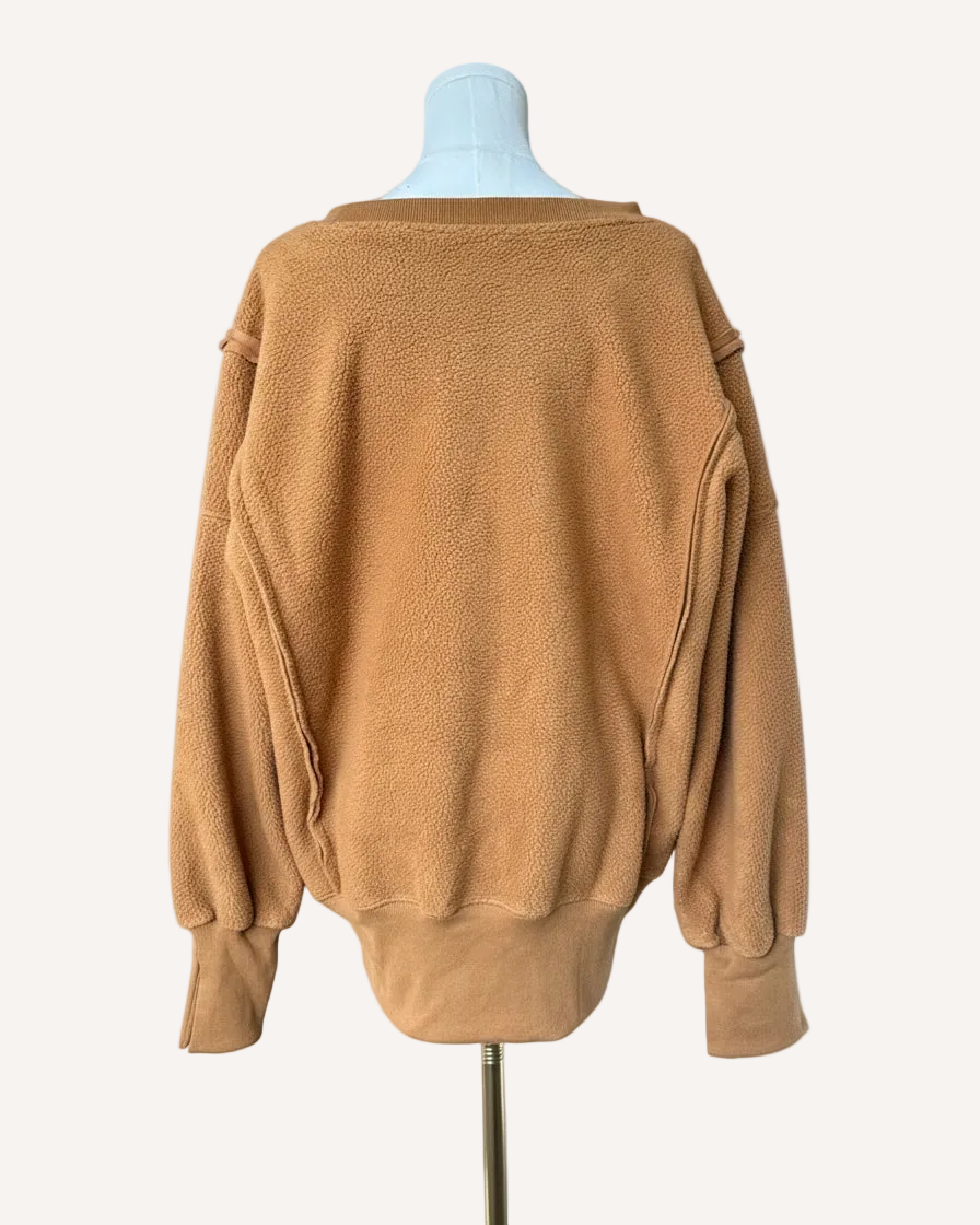 Soft fleece pullover with a relaxed fit, dropped shoulders, and reverse seam detailing, shown in a neutral tone against a clean soft-linen background.