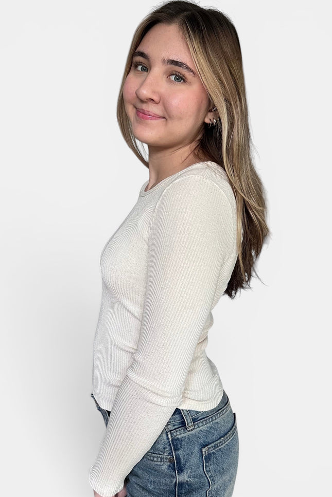 Cream-colored ribbed long-sleeve knit sweater and blue jeans against a plain white studio background.