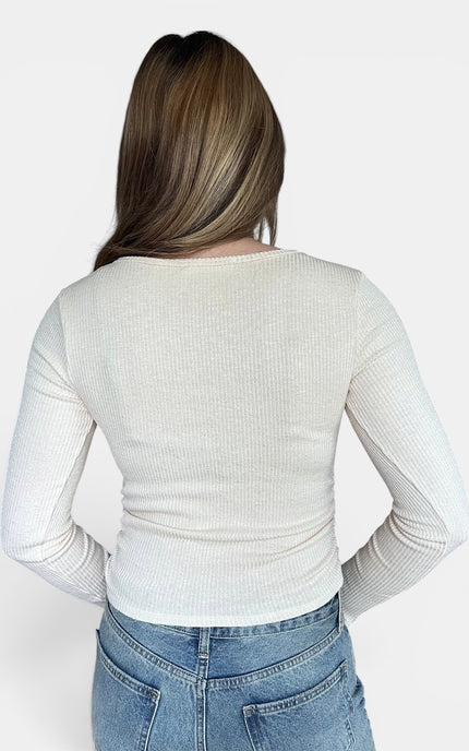 Back view of off-white ribbed long-sleeve top and blue jeans, posing against a solid light gray background.