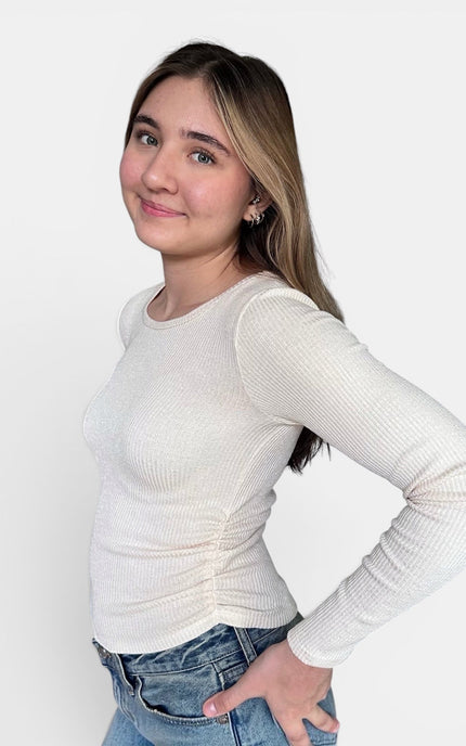 Off-white ribbed long-sleeve top and blue jeans, posing against a solid light gray background.