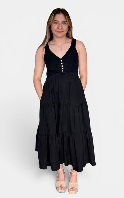 Black sleeveless tiered maxi dress with a V-neckline and decorative buttons down the bodice, paired with beige platform sandals, against a light gray studio background.