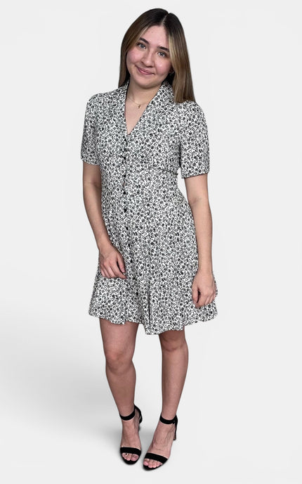 Short-sleeve button-front dress with an allover black and white floral print, paired with black heeled sandals, against a light gray studio background.