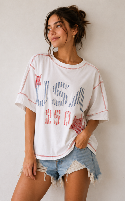Woman wearing a white t-shirt with 'USA 250' print and denim shorts against a plain background