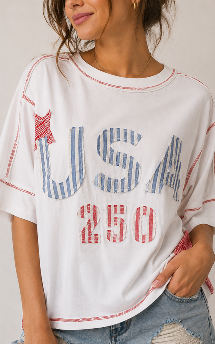Person wearing a white t-shirt with 'USA 250' print and denim shorts on a plain background