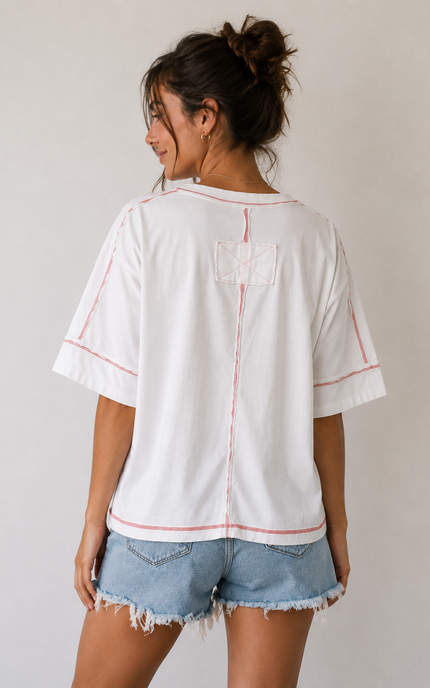 Woman wearing a white t-shirt with red stitching and denim shorts on a plain background