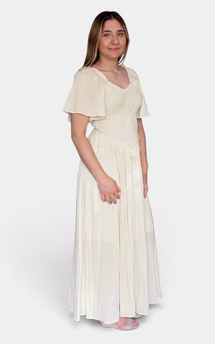 A woman modeling a cream-colored maxi dress with short flutter sleeves, a V-neckline, and a pleated skirt, photographed against a light gray studio background.