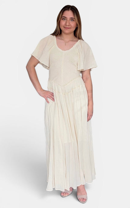 A woman modeling a cream-colored maxi dress with short flutter sleeves, a scoop neckline, and a pleated skirt, set against a plain light gray studio background.