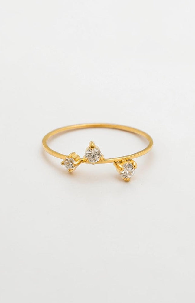 A minimalist flat lay of a delicate 18k gold three-stone CZ ring resting on a clean, soft background, showcasing its timeless and romantic aesthetic.