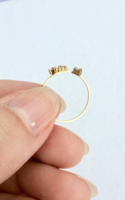 A close-up view of a thin 18k gold PVD plated ring held gently in the palm of a hand, showcasing three sparkling cubic zirconia stones in a delicate prong setting.