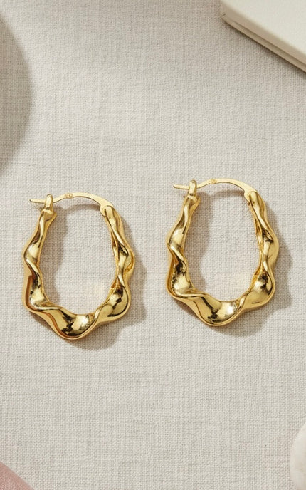 Gold hoop earrings on a light beige fabric background