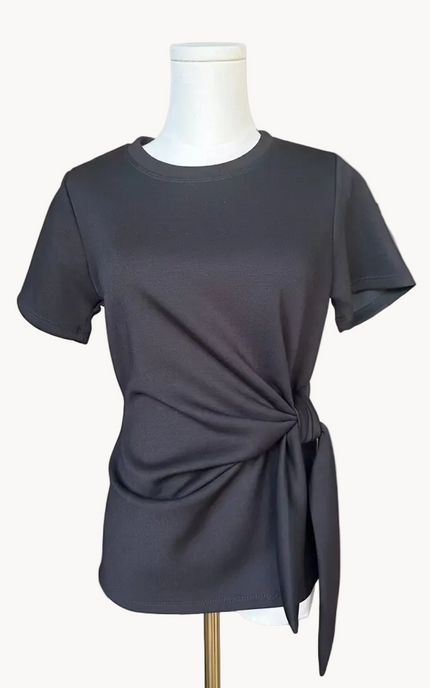 Black top with knot detail on a mannequin against a light pink background