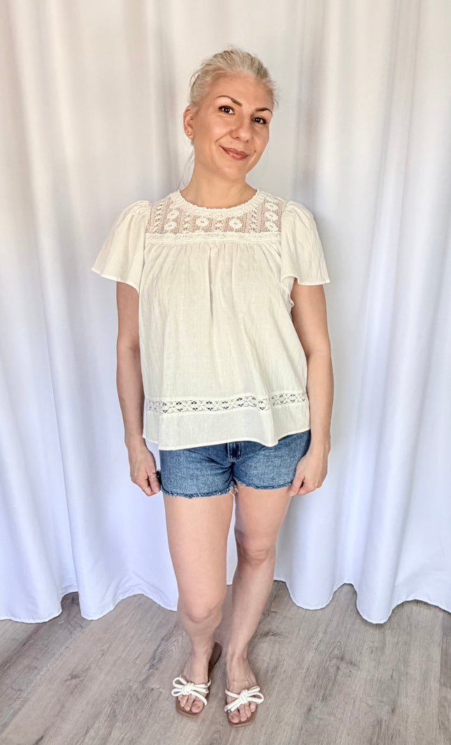 Front view of a model wearing the white cotton Aurelia blouse tucked loosely into high-waisted bottoms, highlighting the flowy drape of the bodice and the delicate placement of the lace yoke.