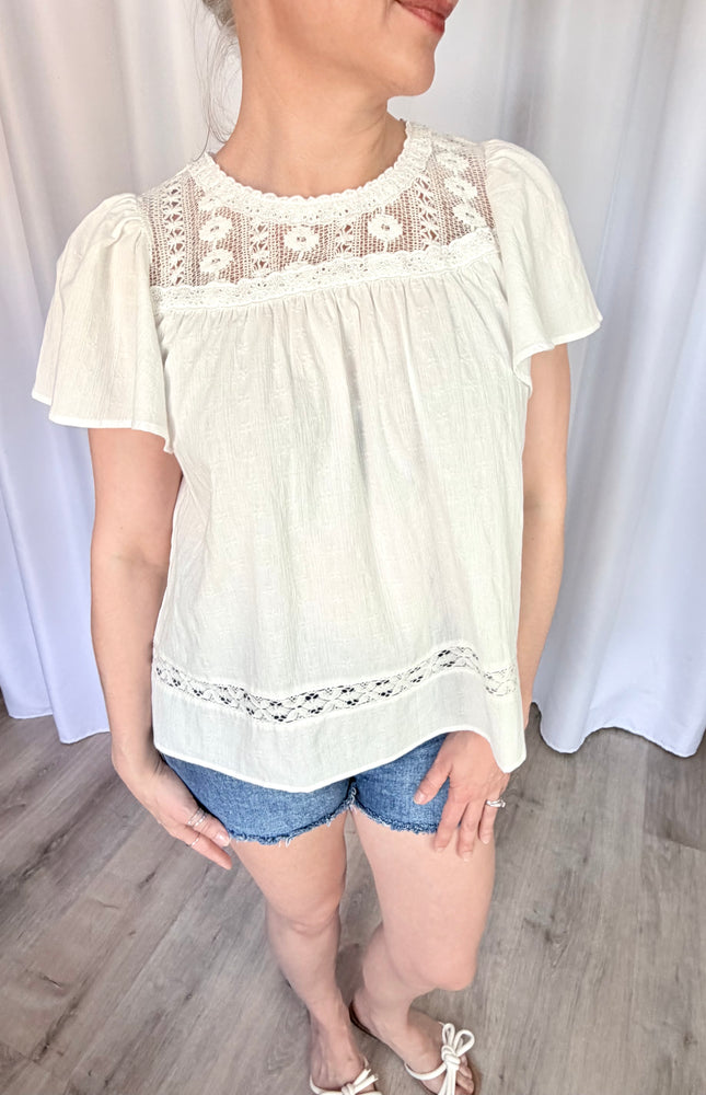 A waist-up front view of the Aurelia blouse, focusing on the romantic combination of the round neckline, intricate vintage lace details, and the soft flare of the short flutter sleeves.
