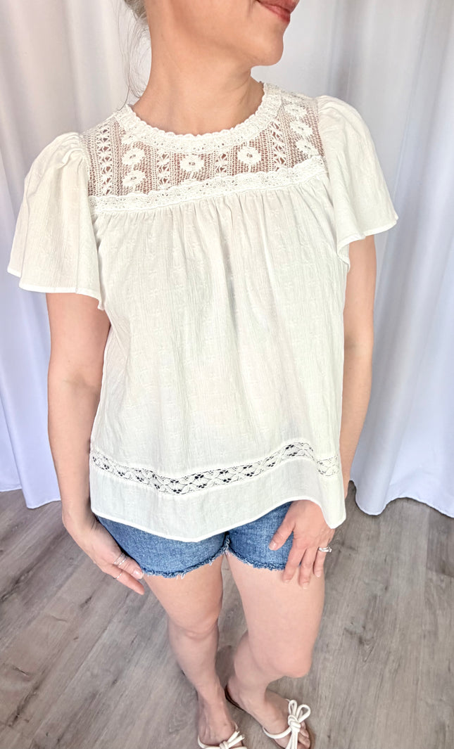 A waist-up front view of the Aurelia blouse, focusing on the romantic combination of the round neckline, intricate vintage lace details, and the soft flare of the short flutter sleeves.