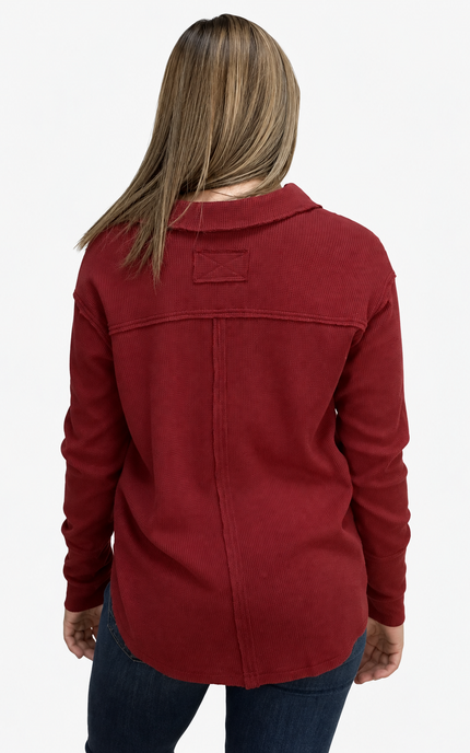 A woman viewed from the back wearing a long-sleeve collared red top and dark blue jeans against a plain white background.