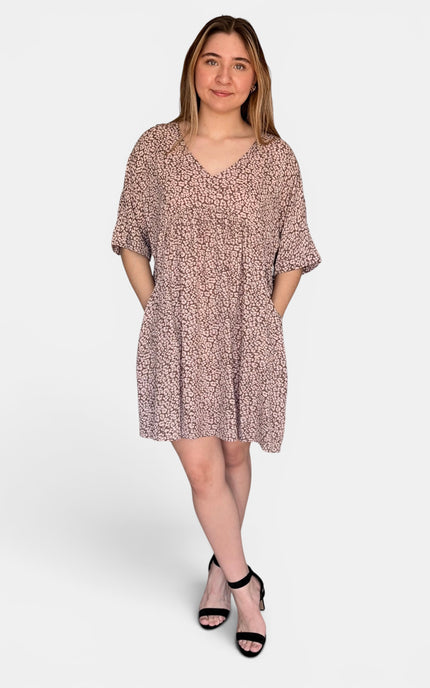 Short-sleeve V-neck dress with an all-over pink and beige abstract print, paired with black heeled sandals, against a light gray studio background.
