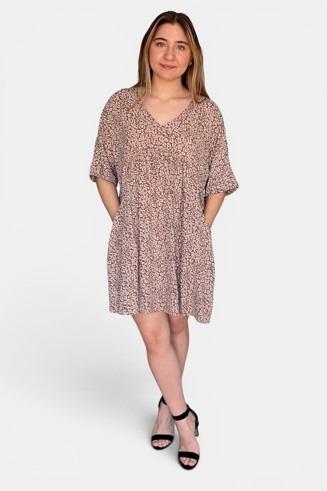 Short-sleeve V-neck dress with an all-over pink and beige abstract print, paired with black heeled sandals, against a light gray studio background.