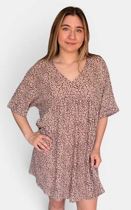 Short-sleeve V-neck dress with a dense small-scale abstract print in dusty pink and brown tones, set against a plain light gray studio background.