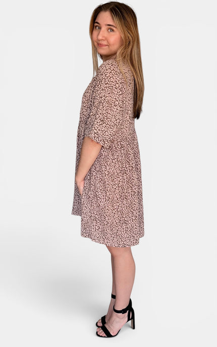 Side view of short-sleeve, knee-length shift dress with a dense small-scale abstract print in dusty pink and beige, paired with black strappy high-heeled sandals against a light gray studio background.