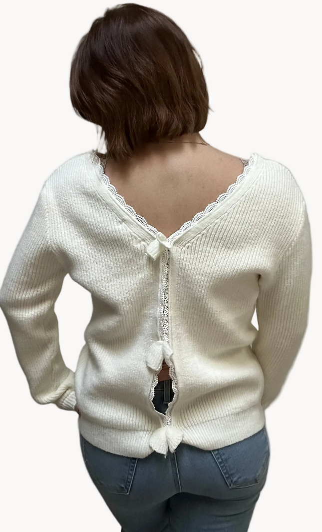 Off-white ribbed sweater with lace-trim V-neckline and oversized bow detail draping down the back, photographed on a Soft Linen background for Justyna Grace Boutique.