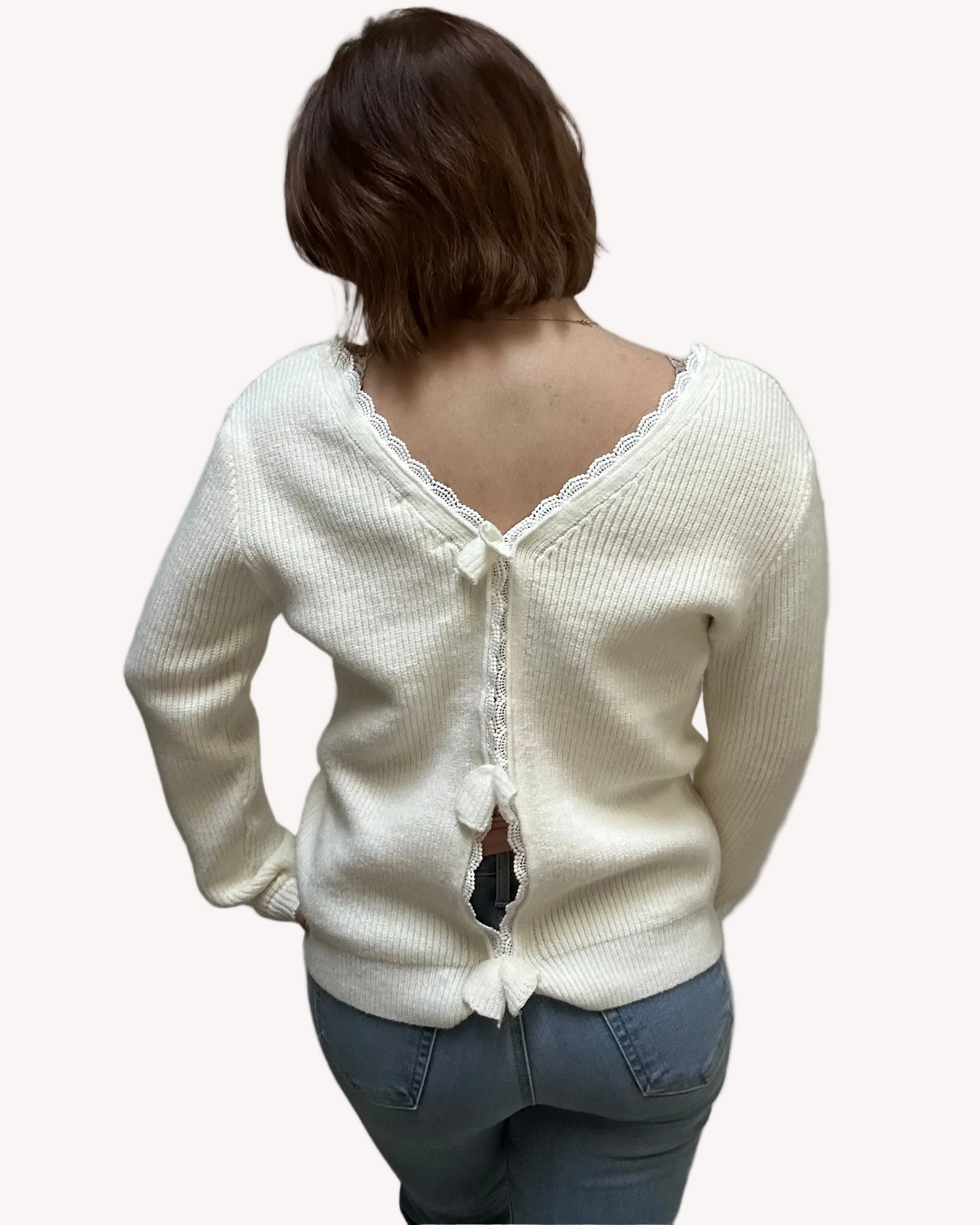 Off-white ribbed sweater with lace-trim V-neckline and oversized bow detail draping down the back, photographed on a Soft Linen background for Justyna Grace Boutique.