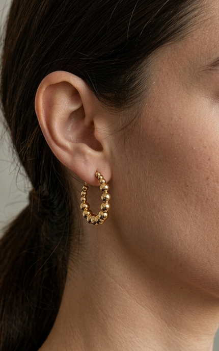 High-detail shot of a woman with dark hair in a low ponytail wearing an 18k gold beaded hoop earring.