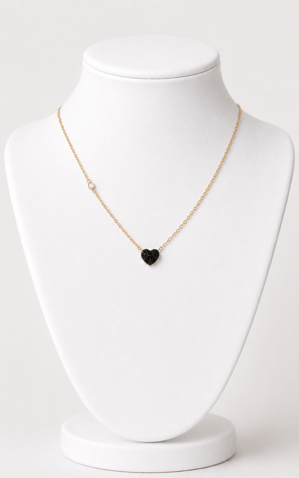 A delicate gold chain necklace with a small black heart-shaped pendant, displayed on a white jewelry bust against a light gray background.