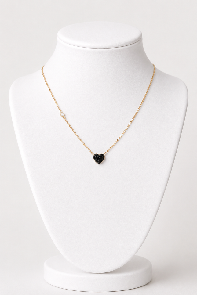 A delicate gold chain necklace with a small black heart-shaped pendant, displayed on a white jewelry bust against a light gray background.