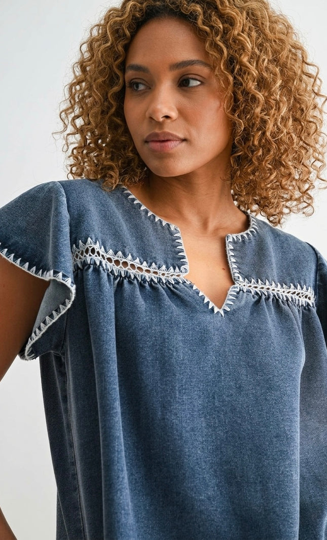 Close-up of white embroidery on the yoke of a Tencel denim blouse.