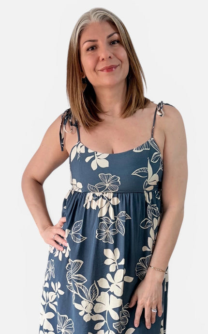 A woman modeling a midnight blue sleeveless dress with an ivory floral pattern against a light gray background.