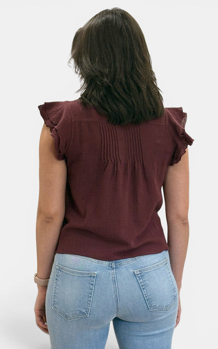 A woman viewed from behind wearing a burgundy ruffled short-sleeve top and light blue jeans against a plain white background.