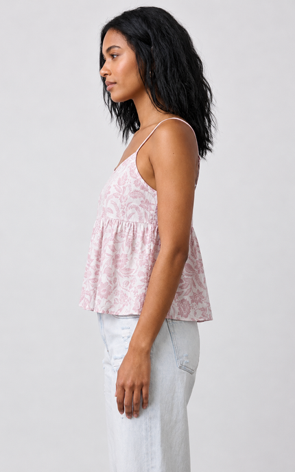 Woman wearing a pink floral top and white pants against a plain background