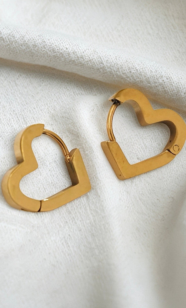 Gold heart-shaped hoop earrings on a white fabric background