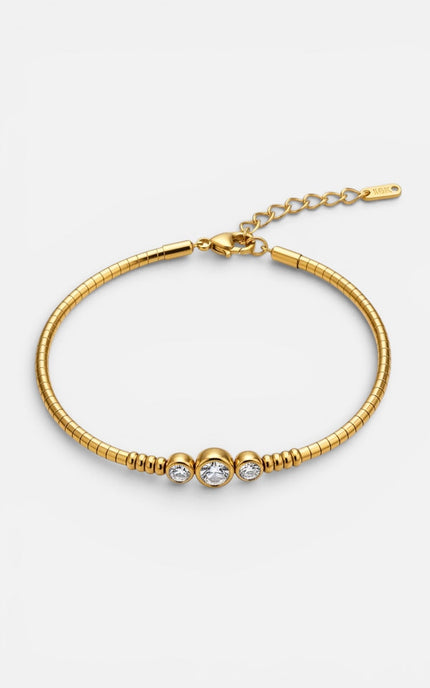 A gold snake chain bracelet with three small clear round-cut gemstones set in a row, featuring a lobster clasp and an adjustable extension chain on a light gray background.