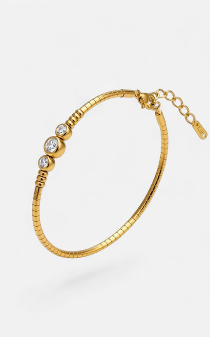 A gold snake-style bangle bracelet with three bezel-set clear round stones and an extender chain, shown on a light gray background.