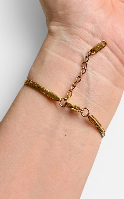A gold-toned textured link bracelet with a chain extender and lobster clasp, shown worn on a person's wrist against a light gray background.