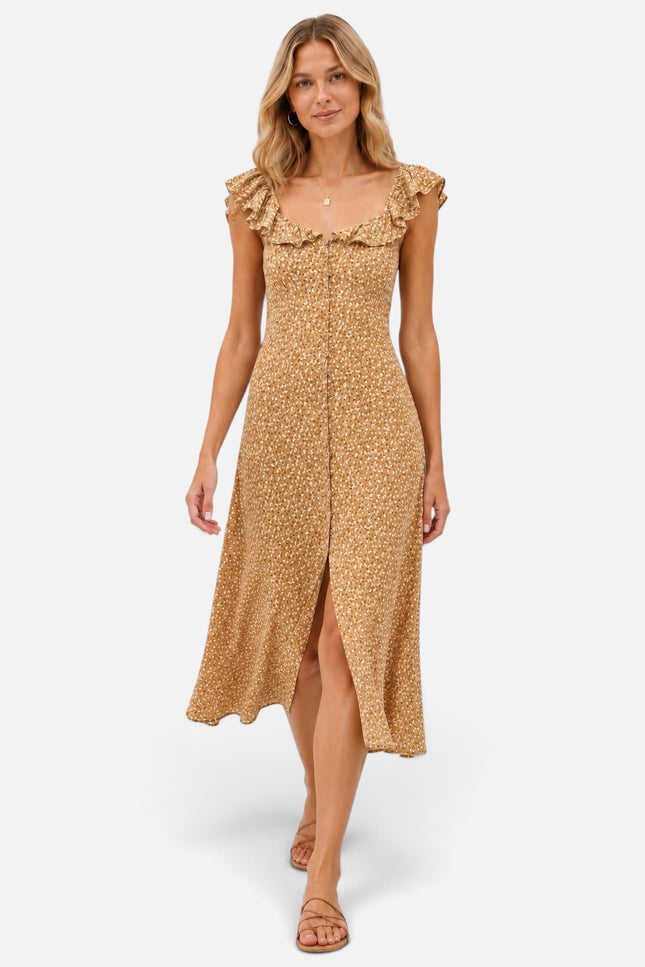 A woman models a sleeveless midi dress with ruffled shoulders and a front slit, against light gray studio background. The dress has a warm tan base with a small repeating floral or ditsy print in a slightly darker golden-brown tone.