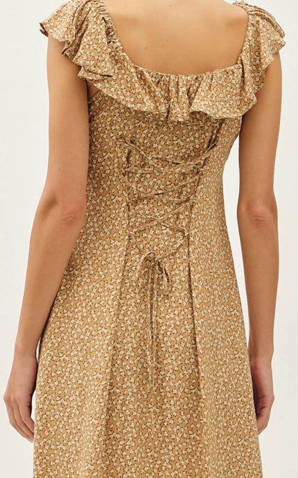 A woman wearing a sleeveless midi dress with a ruffled neckline, lace-up back, and a small-scale floral print in beige and brown tones, shown from the back against a plain light background.