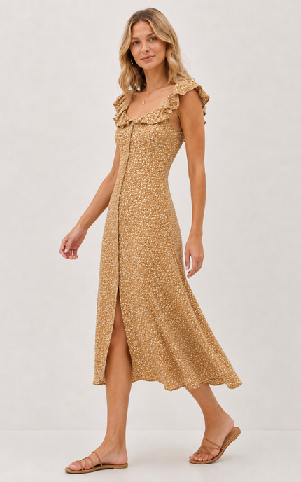 A woman modeling a sleeveless midi dress with ruffled shoulder straps, a square neckline, and a side slit. The dress has a warm tan base with a small-scale beige and brown floral or ditsy print.