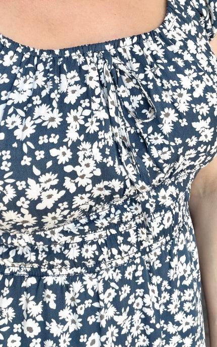 Close-up of a sleeveless top or dress with a navy blue and white floral print, featuring a smocked bodice and tie detail at the neckline.