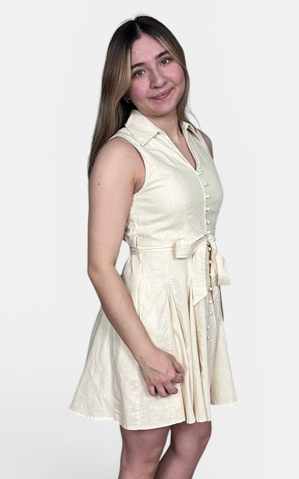 Sleeveless cream-colored mini dress with a collared neckline, button front, and self-tie waist belt, photographed against a plain light gray background.