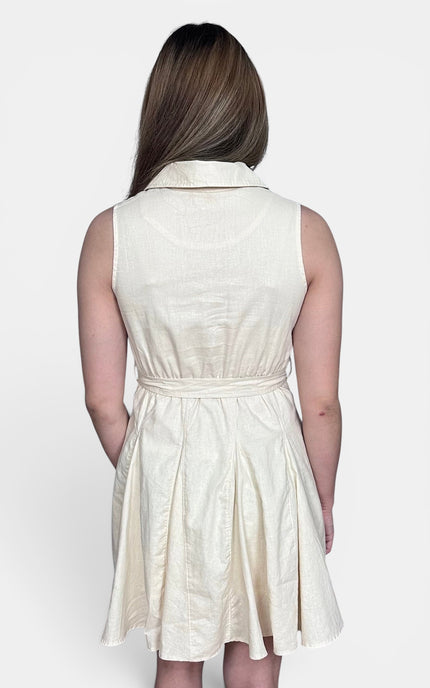 A woman viewed from the back wearing a sleeveless cream-colored dress with a collar, waist tie, and flared skirt, set against a plain light gray background.