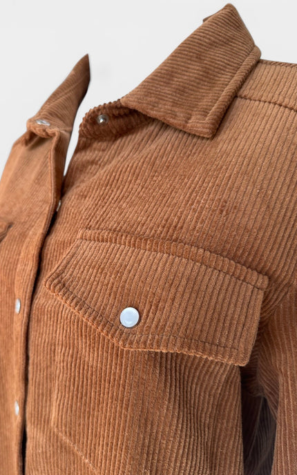 Close-up of a brown corduroy button-up shirt jacket with a pointed collar and a chest pocket, shown on a plain light background.