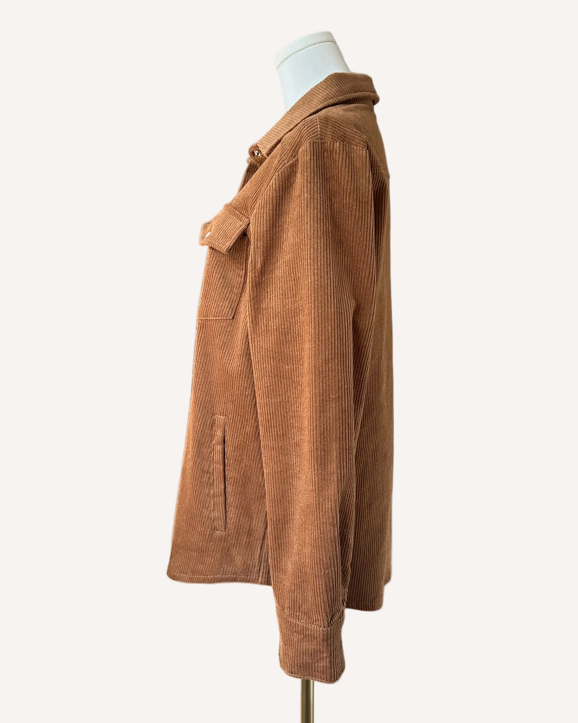 Soft corduroy button-down shacket with a relaxed fit and side pockets, shown in a neutral tone against a clean soft-linen background, styled as a cozy layering piece.