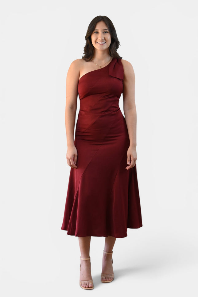 Woman wearing a cranberry one shoulder midi dress with statement bow, fitted bodice, and flared skirt.