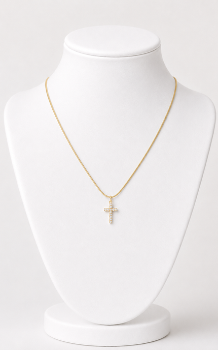 A delicate gold chain necklace with a small cross pendant adorned with clear stones, displayed on a white jewelry bust against a light gray background.
