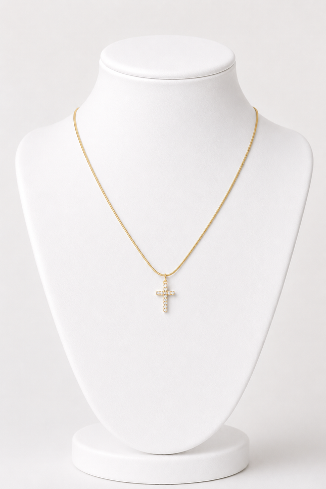 A delicate gold chain necklace with a small cross pendant adorned with clear stones, displayed on a white jewelry bust against a light gray background.