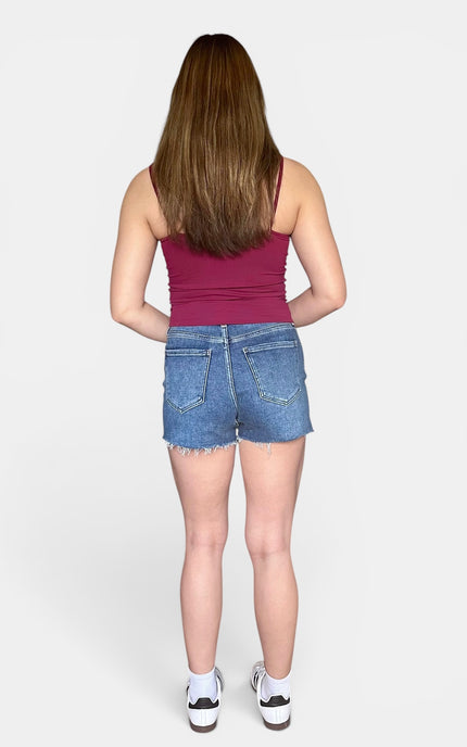 Back view of medium-wash denim shorts with a raw cut-off hem and classic pockets.