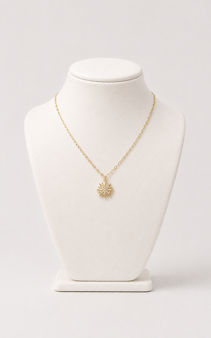 A delicate gold chain necklace with a small sunburst pendant, displayed on a white jewelry bust against a light gray background.